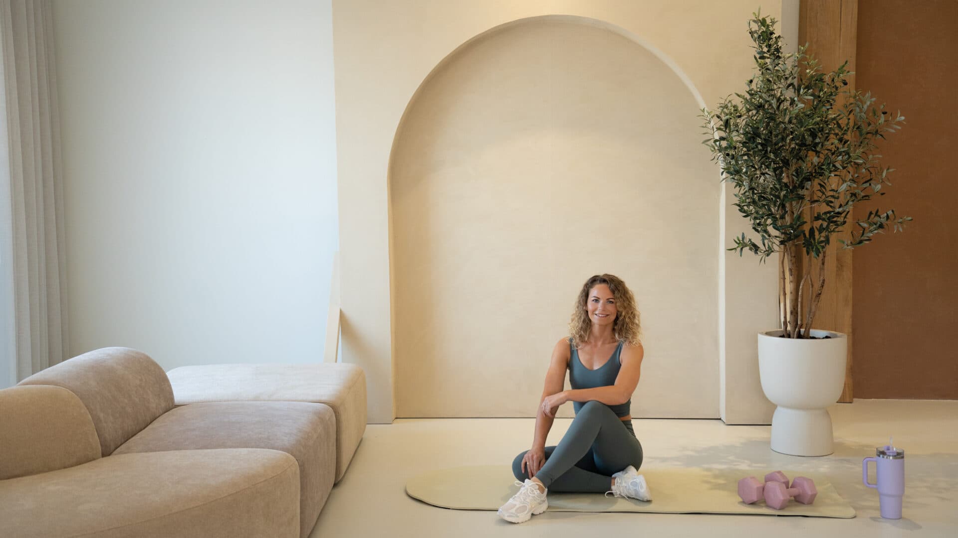 Marlou zittend op een mat in een serene crème studio met een boognis